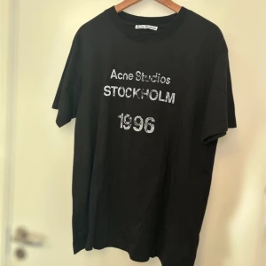 Svart t-shirt från Acne Studios - Snygg svart t-shirt från Acne Studios med texten 'STOCKHOLM 1996' i vitt på framsidan. Perfekt för en stilren och modern look.