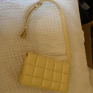 axelväska från Monki - Snygg beige axelväska från Monki. Väskan har en justerbar axelrem och en praktisk dragkedja inuti för säker förvaring. Perfekt för att ge din outfit en stilren touch.