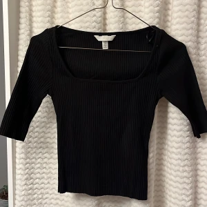 Svart ribbad topp från H&M🖤 - Säljer en stilren svart ribbad topp från H&M med trekvartsärm och en fyrkantig halsringning. 🐝