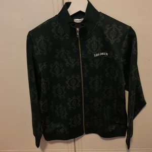 Mönstrad jacka från Les Deux - Snygg mörkgrön jacka från Les Deux med ett unikt mönster. Jackan har dragkedja framtill och ribbade muddar vid ärmslut och krage. Perfekt för en stilren look.