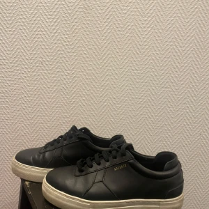 Svarta sneakers från Axel Arigato - Snygga svarta sneakers från Axel Arigato i skinn med klassisk snörning. Skorna har en vit sula som ger en stilren kontrast. Perfekta för en avslappnad och trendig look.