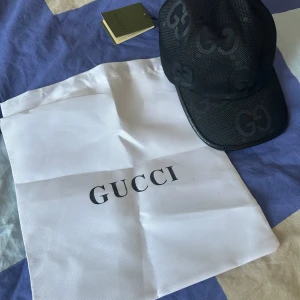 Svart keps från Gucci - Snygg svart keps från Gucci med det ikoniska GG-mönstret. Kepsen har en klassisk design och är perfekt för att ge en lyxig touch till din outfit. Den kommer med en vit förvaringspåse med Gucci-logotypen.