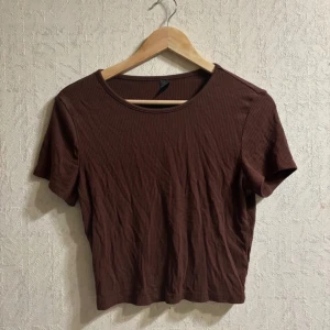 Brun ribbad t-shirt - Den är lite nopprig. En brun ribbad t-shirt med korta ärmar. Perfekt för en avslappnad stil. T-shirten har en rund halsringning och är gjord i ett mjukt material.