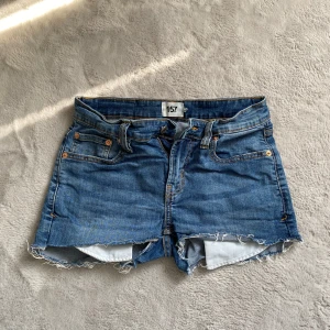 Blå jeansshorts från 157 - Säljer ett par snygga blå jeansshorts från 157. De har en klassisk femficksdesign och fransiga kanter för en avslappnad look. Perfekta för sommardagar!
