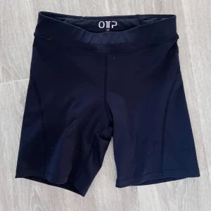 Svarta träningsshorts från OTP - Säljer ett par svarta träningsshorts från OTP i storlek XS.(32-34) De är tillverkade i ett stretchigt syntetmaterial och har en tight passform som passar perfekt för träning. 