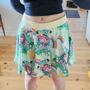 Färgglad kjol med tecknat motiv - Säljer en färgglad kjol med ett unikt tecknat motiv av regnbågar och figurer. Kjolen har en bekväm passform och är perfekt för dig som vill sticka ut. Den är gjord i ett mjukt material och har en dragkedja i sidan.