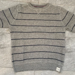 Grå randig tröja från gant - Säljer en stilren grå tröja från Le Mont St Michel med mörkblå ränder. Tröjan har en klassisk rund hals och korta ärmar, perfekt för en avslappnad look. Den är tillverkad i ett mjukt material som ger en bekväm passform.