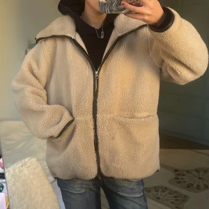Beige teddyjacka med dragkedja - Mysig beige teddyjacka från arket med dragkedja framtill. Jackan har en avslappnad passform och långa ärmar. Läder detaljer! 