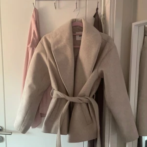 Beige kappa med bälte - Säljer en  beige kappa med bälte. Perfekt nu till våren.  Kappan är enkel att matcha och inte mycket använd då för liten. 