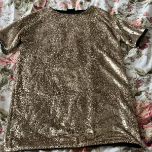 Guldig paljettklänning från KappAhl - Säljer en glittrig guldig klänning från KappAhl i storlek M. Klänningen har korta ärmar och är täckt av paljetter som ger en riktigt festlig look. Perfekt för dig som vill sticka ut och glänsa på nästa tillställning!