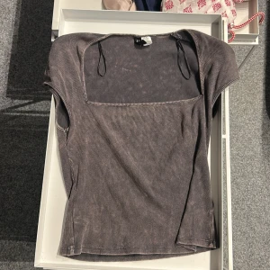 Grå ribbad topp från Divided - Säljer en grå ribbad topp från Divided med fyrkantig ringning och korta ärmar. Toppen har synliga sömmar och en tight passform, perfekt för en trendig och avslappnad look.