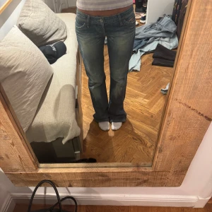 Blå bootcut jeans från Replay - Säljer ett par klassiska blå bootcut jeans från Replay med normal passform. Jeansen har fem fickor, dragkedja och knapp framtill samt snygga detaljer på bakfickorna. Perfekta till vardags och lätta att matcha.