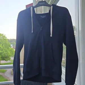 Mörkblå hoodie med dragkedja - Mörkblå hoodie från Bondelid med vit dragsko och dragkedja framtill. Klassisk modell med långa ärmar och fickor på sidorna. Perfekt för en avslappnad stil. Pris går att diskuteras