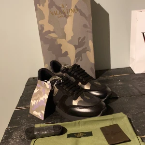 Valentino Rockrunner sneakers med camouflage - Säljer ett par Valentino Rockrunner sneakers med svart och grön camouflage-mönster. Skorna har svarta snören, rund tå och detaljer i skinn. Kommer med extra skosnören och dustbag. Perfekta för dig som vill sticka ut med stil.