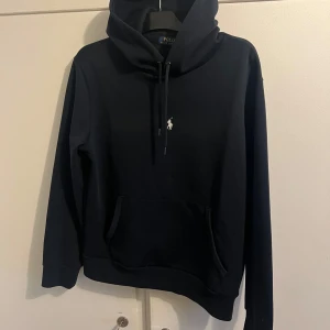 Mörkblå hoodie från Polo Ralph Lauren - Säljer en mörkblå  hoodie från Polo Ralph Lauren med klassisk logga broderad på bröstet. Tröjan har huva med dragsko och en stor magficka framtill. Perfekt för en avslappnad och stilren look. Pris kan diskuteras!