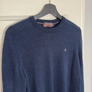 Mörkblå stickad tröja från Morris - Säljer en mörkblå stickad tröja från Morris i 100% merinoull. Tröjan har rund halsringning, diskret logga broderad på bröstet och långa ärmar. Perfekt för lager-på-lager och stilren look.