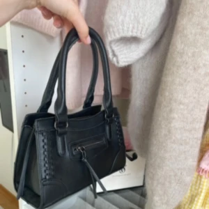 Svart väska med ditaljer  - Såå fin väska med ditaljer! Perfekt stolek för det viktigaste och enkel att matcha till olika outfits. Knappt andvänd då den är andvänd cirka 2-3 gånger, inga defekter! Hör av er om ni har fler frågor💕💕 Höjd: ca 14 cm, bred: ca 20 cm💕 (följer med band till väskan).