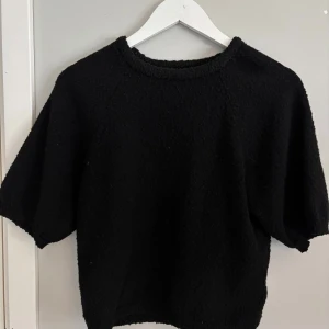 Svart stickad tröja från Lindex - Mysig svart stickad tröja från Lindex med korta ärmar och rund halsringning. Perfekt för lager-på-lager och enkel att matcha med olika outfits. Säljes i storlek S.