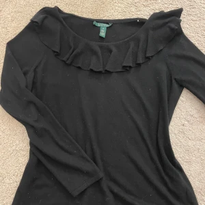 Ralph lauren tröja - En svart Ralph Lauren tröja med volanger💕Ganska lång nertill men fortfarande jättefin. Säljer för den inte kom till användning. Storlek står inte riktigt men passar nog allt från small till large 