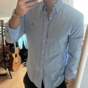 Polo Ralph Lauren skjorta - Säljer denna klassiska ljusblå skjorta från Polo Ralph Lauren. Skjortan har knappt varit använd därav så är skicket 10/10, den har inga fläckar eller andra flaws. Storleken är M och han i bilden är 180cm lång och väger 70kg. Priset är diskuterbart. Det är bara att höra av er vid eventuella frågor. Mvh, Hjalmar