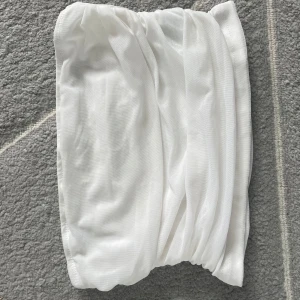 Vit tubtopp i mjukt material - Säljer en enkel och stilren vit tubtopp i mjukt och stretchigt tyg. Perfekt att matcha med jeans eller kjol för en clean look. Toppen är axelbandslös och har en lätt rynkad effekt på sidorna.