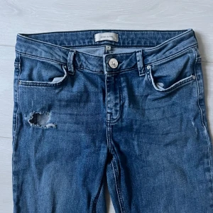 Blå bootcut jeans från River Island - Säljer mina absolut favorit jeans som blivit för små för mig ett par blå bootcut jeans från River Island med slitningar på vänster lår. Klassisk femficksmodell med knapp och dragkedja. Perfekta för dig som gillar en avslappnad och trendig look. Jeansen har slitage på slutet av längderna då dem är ganska långa, men går enkelt att klippa bort själv och anpassa till sin egen längd☺️KOLLA SISTA BILD FÖR HUR DEM SER UT PÅ!