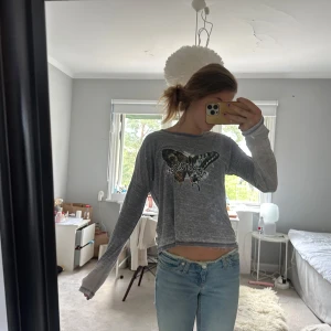 Grå croppad långärmad tröja med fjärilstryck - Säljer en grå långärmad tröja med stort fjärilstryck och text framtill. 