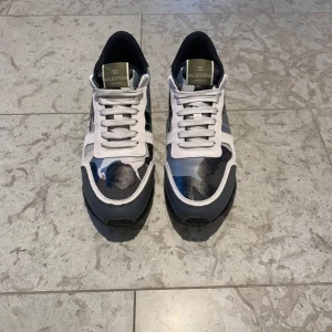 Valentino Rockrunner sneakers med camomönster - Säljer ett par Valentino Rockrunner sneakers med grått, svart och vitt camomönster. Skorna har snörning, rund tå och platt sula. Märkesdetaljer på plösen och klassisk design som sticker ut. Skorna är i 9/10 skick och nästan sprillans nya. 