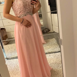 Ljusrosa långklänning med paljetter - Säljer en ljusrosa långklänning med glittrig paljettöverdel och öppen rygg i snygg oneshoulder-modell. Kjolen är mjukt fallande och klänningen har en elegant siluett som verkligen sticker ut. Perfekt för bal eller student!