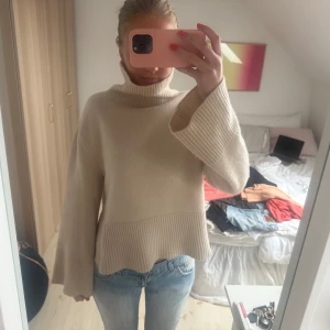 Beige stickad polotröja - Säljer en beige stickad polotröja med breda ärmar och ribbade detaljer vid nederkant och ärmslut. Tröjan har en hög polokrage och en loose passform. Supermjuk och stilren, passar till allt!