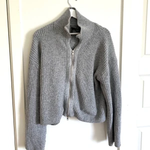 Grå stickad tröja med dragkedja - Klockren stickad tröjan inför årets sommarkvällar! Lite oversized utan att bli pösig och med en stilren silvrig dragkedja! Ett måste för alla att ha i garderoben.