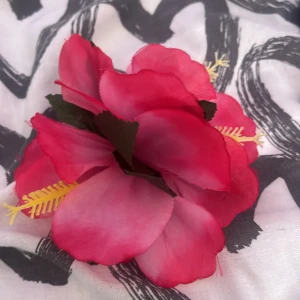 Rosa blomklämma  - Snyggt hårklämma  med stora rosa hibiskusblommor och gröna blad. Perfekt accessoar för sommarens fester eller temakvällar. Blommorna är i tyg och diademet har en metallklämma på baksidan för enkel fastsättning i håret.
