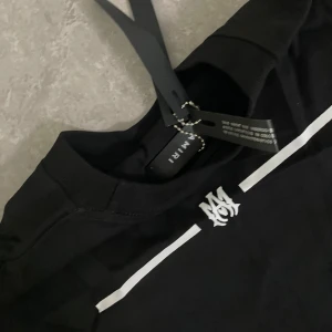 Amiri t shirt  - Snygg svart t-shirt från Amiri med vit logga på bröstet och ett diskret vitt tryck över bröstet. Klassisk rund halsringning och korta ärmar. Perfekt för en stilren och trendig look.