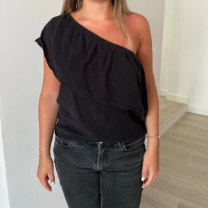 Svart oneshoulder topp - Säljer en svart oneshoulder topp från H&M med lös passform och volangdetalj över axeln🫶🏽 Toppen är i storlek 44 men jag skulle säga passar för storlek 38-40 då den är liten i storlek🫶🏽