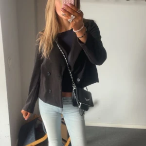 Svart kappa från NA-KD - Säljer en svart kappa från NA-KD med dubbelknäppning och klassisk krage. Jackan har lång ärm och en rak, något kortare passform som ger en modern look. Perfekt att styla med jeans eller kjol. Använd fåtal gånger men inget tydligt tecken på slitage.