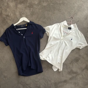 Pikétröjor från Polo Ralph Lauren - Köpta tillsammans för 1300kr, eller styck!  klassiska pikétröjor från Polo Ralph Lauren, en i marinblått med röd logga och en i vitt med marinblå logga. Båda har kort ärm, krage och knappar framtill. Perfekta för en stilren och sportig look.