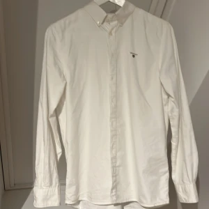 Vit skjorta från GANT - Klassisk vit skjorta från GANT med broderad logga på bröstet. Skjortan har lång ärm, knappar hela vägen och en stilren krage. Perfekt för dig som gillar en clean och tidlös look. KAN PRUTA!!!!
