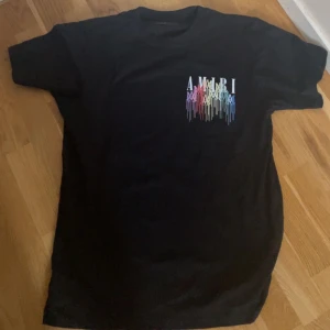 Svart t-shirt från Amiri med färgglatt tryck - Svart t-shirt från Amiri med färgglatt, droppande logotyptryck på bröstet och ryggen. T-shirten har rund hals och normal passform. Perfekt för dig som gillar streetwear och vill sticka ut med en unik design. Ingen användning på den så den är sprillans ny för dig som söker en riktigt snygg t-shirt 