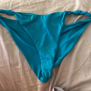 Turkosa bikiniunderdel från Lindex  - Säljer en turkos bikiniunderdel från Lindex i storlek L. Modellen har högt skurna ben och coola knutdetaljer på sidorna. Tillverkad i återvunnen polyesterblandning som känns mjuk och följsam mot huden. Perfekt för strandhäng och poolparty!