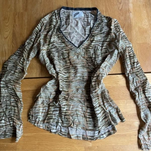 Zebramönstrad meshblus med v-ringning - Säljer en transparent zebramönstrad meshblus i beige, brun och vit med v-ringning och långa ärmar. Blusen har små broderade tjurhuvuden i mönstret. Perfekt för dig som gillar unika prints och coola detaljer.