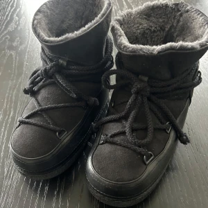  Inuikii, strl 37, svarta i mocka o skinn  - Moon boots från Inuikii i svart mocka och skinn med fluffigt ylle foder och grov gummisula. Snygga snörningsdetaljer runt hela skon och rund tå. Perfekta för kalla vinterdagar när du vill hålla stilen och värmen. Fin beg.skick