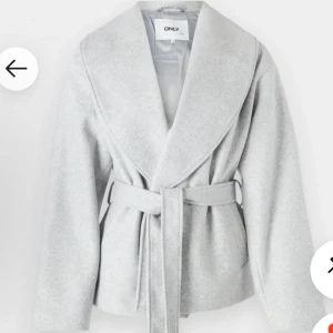 Ljusgrå omlottjacka från ONLY - Snygg ljusgrå omlottjacka från ONLY med bred krage och bälte i midjan. Jackan har lång ärm och är tillverkad i mjukt ullblandat material. Perfekt för dig som gillar stilrena och trendiga plagg med en clean look.