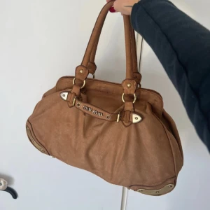 Miu Miu väska - AS snygg vintage Miu Miu väska som jag har köpt från en tjej på Vinted Hon som jag köpte den av påstår att den är äkta, hon köpte den på en vintage flea market i Italien. Hon hade dock inget kvitto eller äkthetsintyg så jag vet inte om den är legit därav säljer jag den så pass billigt. Oavsett är den fruktansvärt snygg☝🏻🤗Känns o vara i något sorts mocka material/imitation. Väskan ser man är gammal så man kan absolut rusta upp den och ge den mer kärlek! Det är även lite skiftningar i tyget💋
