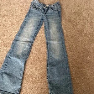 Blå bootcut jeans från Gina Tricot - Snygga ljusblå jeans från Gina Tricot i storlek 152. Modellen har klassisk bootcut och fem fickor, med slitningar och tvättade detaljer för en cool look. Jeansen är tillverkade i jeansmaterial och har knapp och dragkedja framtill.