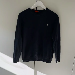 Mörkblå merinoulltröja från Morris - Mörkblå långärmad tröja från Morris i 100% merinoull. Klassisk rund hals och diskret Morris-logga broderad på bröstet. Tröjan har en stilren och enkel design med ribbade muddar vid ärmslut och nederkant. Skriv vid frågor/funderingar 😁