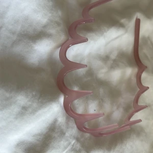 Rosa vågigt diadem i plast - Säljer ett unikt diadem i ljusrosa plast med vågig form och spetsiga detaljer. Perfekt för att ge din frisyr en cool och lekfull touch. Diademet är lätt och sitter bekvämt på huvudet. Passar dig som vill sticka ut med en trendig accessoar.