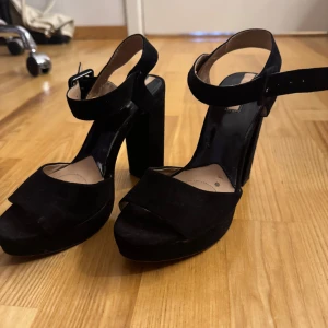 Svarta mocka klackskor med platå - Snygga svarta klackskor från Stradivarius i mocka med breda remmar och justerbart spänne runt ankeln. Skorna har hög blockklack och platåsula, samt öppen tå. Kan ej ta bild på eftersom dom ej passar💗
