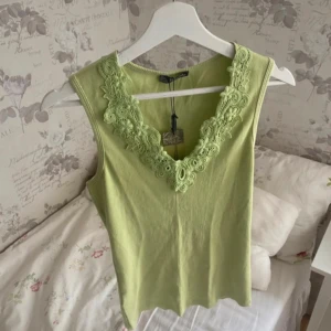 Ljusgrön ribbad linnetopp med spets - Superfin ljusgrön linnetopp med v-ringning och bred spetskant framtill. Toppen är ribbad och ärmlös, perfekt för varma dagar. Sitter snyggt och har en fräsch, somrig vibe. Passar till både jeans och kjol för en chill look. Strl L men passar både S & M med! Ny med prislapp kvar! Nypris 199kr