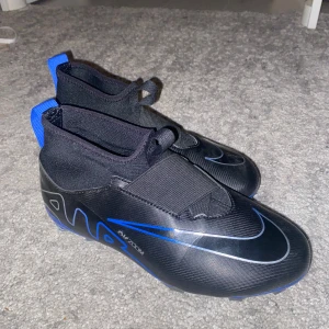 Nike Air Zoom svarta/blå fotbollsskor - Snygga Nike Air Zoom fotbollsskor i svart med blå detaljer och silverfärgad swoosh. Skorna har en strumpliknande passform, låg vikt och mönstrad sula med dobbar för bra grepp på planen. Perfekta för dig som vill sticka ut på matchen! Har aldrig använt det max 1 gång!