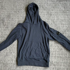 Mörkblå hoodie från C.P. Company - Mörkblå hoodie från C.P. Company i storlek 152/ 12 år. Tröjan har huva och magficka. Den är i bra skick. Priset är förhandlingsbart.
